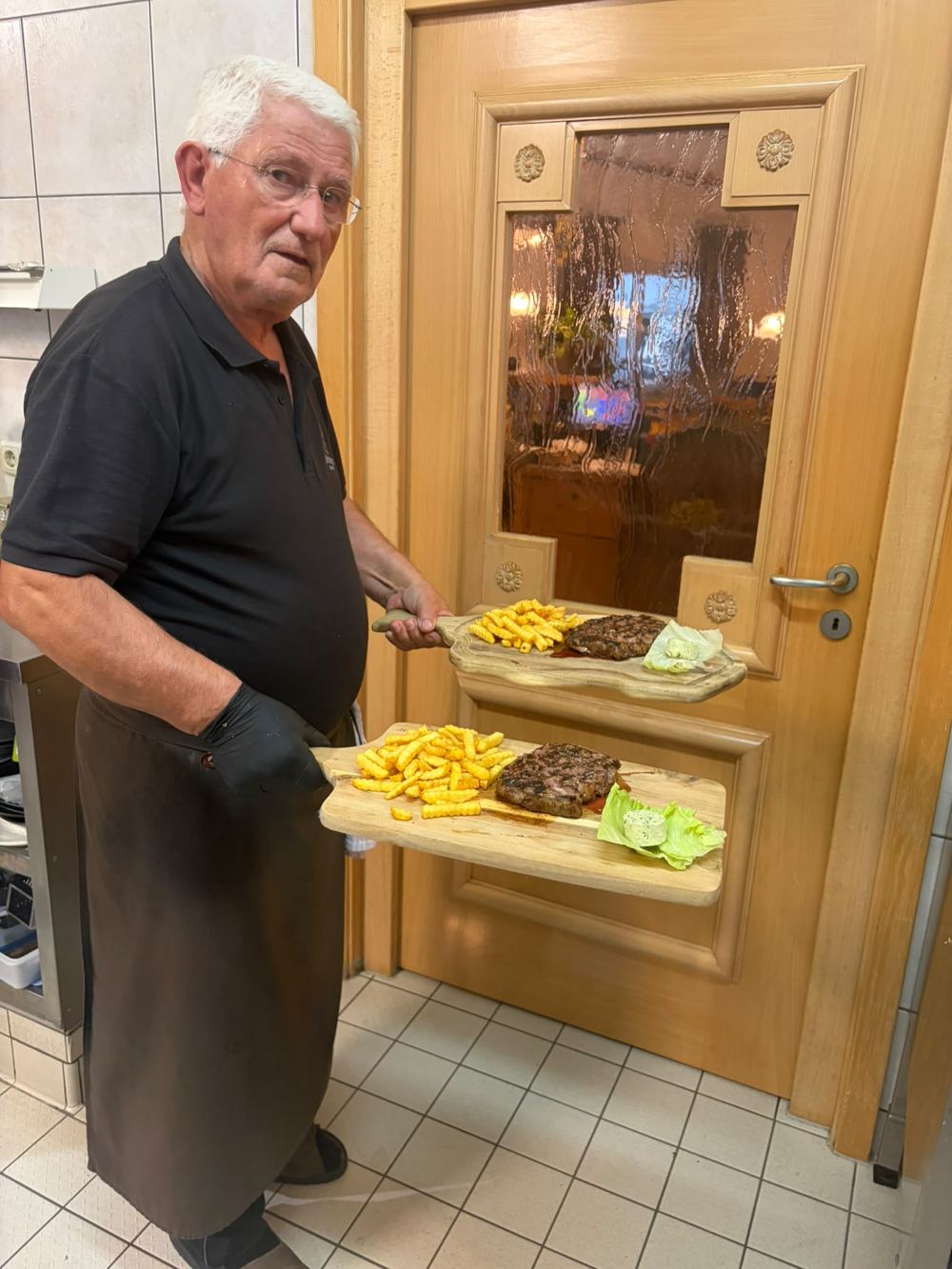 Zwei Holzbretter mit Grillgericht werden an den Tisch gebracht